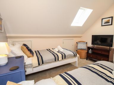 A bedroom with two single beds a blue bedside table with a lamp a television on a wooden stand and a skylight at Blanche Cottage Brewers Quay Harbour