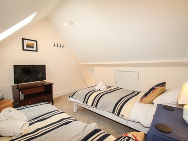 A bedroom with two single beds a television on a wooden stand and a skylight at Blanche Cottage in Brewers Quay Harbour