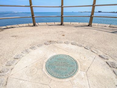 A circular stone platform with a metal plaque and railing overlooking the sea at Blanche Cottage in Brewers Quay Harbour