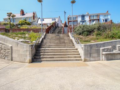 A set of concrete stairs with metal handrails leading up to residential houses with gardens