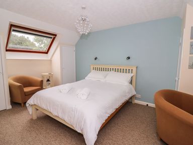 A bedroom with a double bed white bedding two brown armchairs a small side table and a skylight window at Oak Tree Cottage in Aberporth