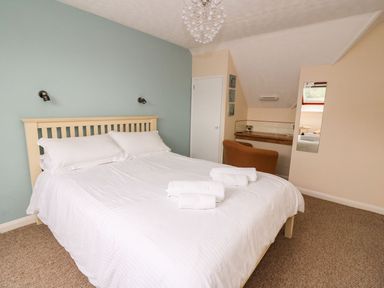 A bedroom with a double bed with white bedding and towels on it a chair a desk a wall mirror and a window at Oak Tree Cottage in Aberporth