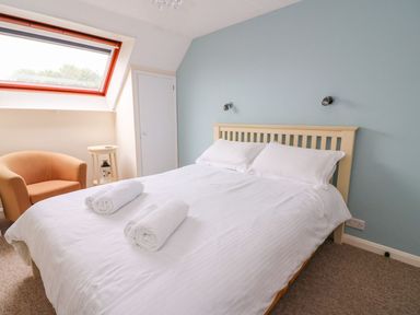 A bedroom with a double bed two rolled towels a beige armchair and a skylight window at Oak Tree Cottage in Aberporth