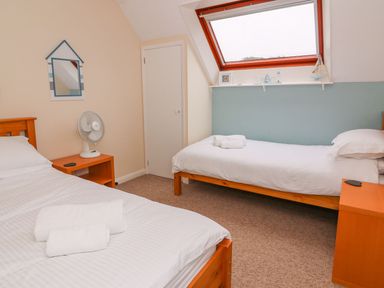 A bedroom with two single beds a small fan on a bedside table and a skylight window at Oak Tree Cottage in Aberporth