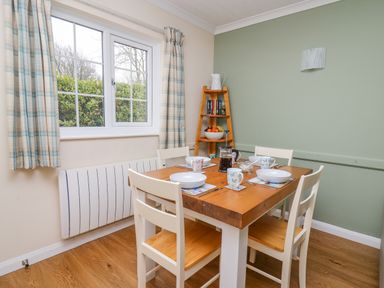 A dining room with a wooden table set for four and a window with checkered curtains at Oak Tree Cottage in Aberporth