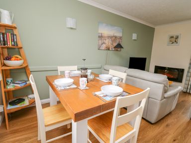 Dining table with bowls and mugs set for four next to a beige sofa and a wall-mounted electric fireplace at Oak Tree Cottage in Aberporth