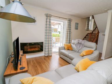 A living room with grey sofas and orange cushions next to a wall-mounted electric fireplace and a television at Oak Tree Cottage in Aberporth