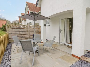 A patio area with a round glass table umbrella four chairs and a wooden fence at Oak Tree Cottage Aberporth