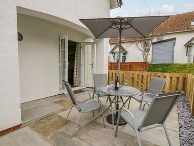 An outdoor patio area with a glass table four chairs and an umbrella at Oak Tree Cottage in Aberporth