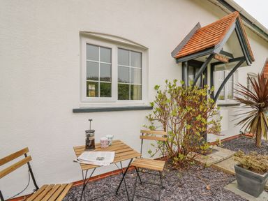 A small outdoor seating area with a wooden table and two chairs outside a white house at Oak Tree Cottage in Aberporth