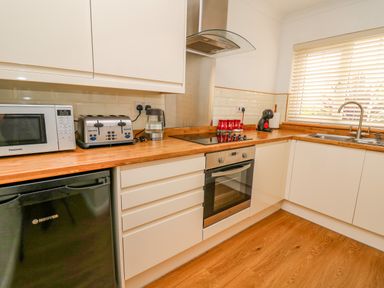 A kitchen with microwave toaster kettle oven stove sink and window blinds at Oak Tree Cottage in Aberporth