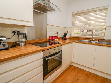 A kitchen with a stovetop oven toaster kettle coffee machine and sink with window blinds at Oak Tree Cottage in Aberporth