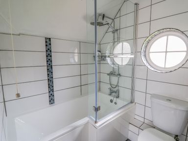 A bathroom with a bathtub shower combination a round window and a toilet at Oak Tree Cottage in Aberporth