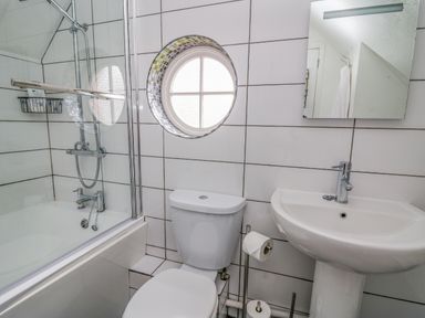 A bathroom with a bathtub shower toilet pedestal sink and round window at Oak Tree Cottage in Aberporth