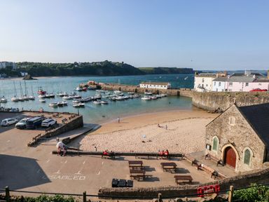 A small harbor with boats moored near a sandy beach and a stone building with benches at Puffins in Tenby