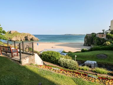 A landscaped garden with benches and flowers overlooking a sandy beach and ocean at Puffins in Tenby