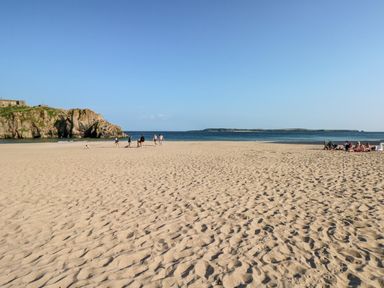 A sandy beach with people near the water and a rocky cliff on the left at Puffins in Tenby