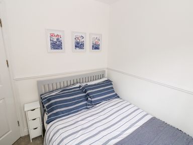 A bedroom with a bed with blue and white striped bedding and three framed pictures on the wall at Puffins in Tenby