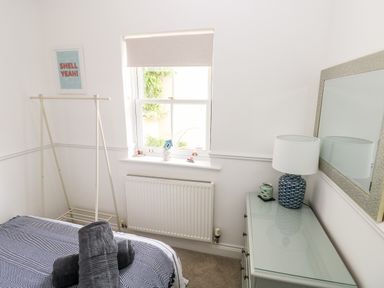 A bedroom with a bed with folded towels a window with a blind a clothes rack a dresser with a lamp and a mirror at Puffins in Tenby