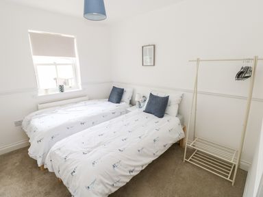 A bedroom with two single beds a window and a clothes rack at Puffins in Tenby