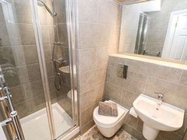 A bathroom with a shower enclosure a wall mounted toilet with a towel on it and a pedestal sink at Puffins in Tenby