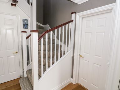 A hallway with carpeted stairs and two white doors with gold handles at Puffins in Tenby