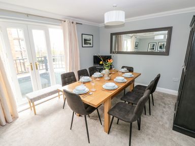 A dining room with a wooden table set for eight and a large wall mirror at Puffins in Tenby