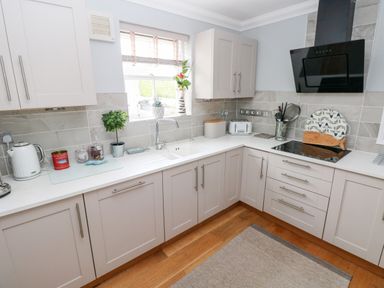 A kitchen with white cabinets a sink toaster kettle and stove at Puffins in Tenby
