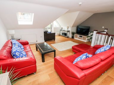 A living room with red sofas blue cushions a black coffee table a television and wooden flooring at Puffins in Tenby