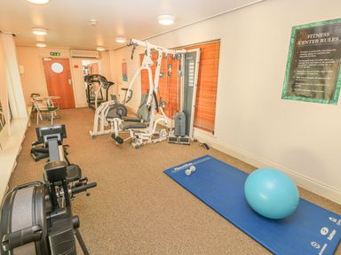 A fitness room with exercise machines a blue mat with a small dumbbell and a blue exercise ball and a wall sign with fitness center rules at Puffins in Tenby