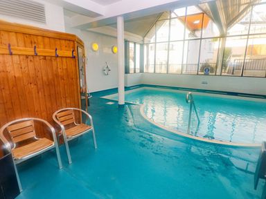 An indoor swimming pool with two chairs and wooden coat hooks on the wall at Puffins in Tenby