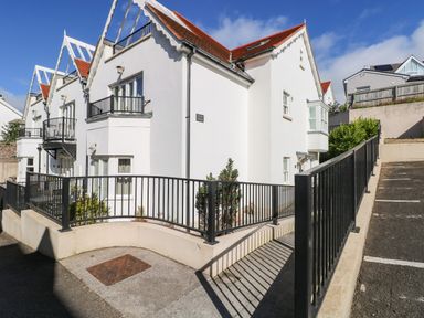 A row of white houses with red roofs and black railings next to a parking area at Puffins in Tenby