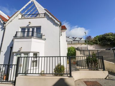 A white house with balconies and black railings under a blue sky at Puffins in Tenby