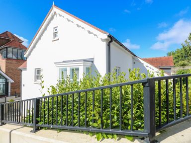 A white house with red roof tiles behind a black metal fence and green bushes at Puffins in Tenby