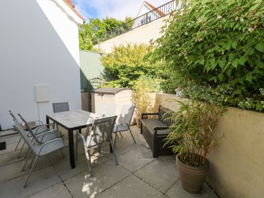 An outdoor patio with a table and six chairs a storage bench and potted plants at Puffins in Tenby