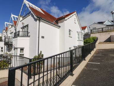 White residential building with red roof and black railing next to a parking area at Puffins in Tenby