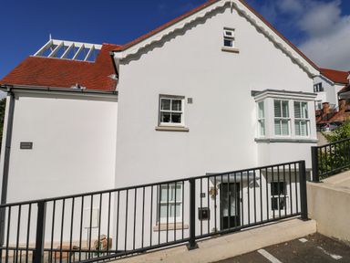 The exterior of a white house with a red roof black railing and windows with white shutters at Puffins in Tenby