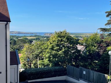 A coastal landscape with trees houses and hills in the background at Puffins in Tenby