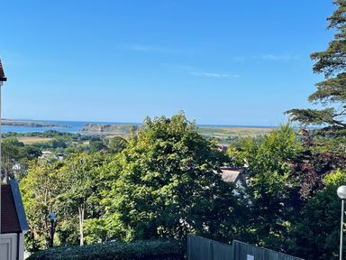 A view of trees and houses with hills and water in the background at Puffins in Tenby