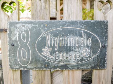 A wooden gate with heart cutouts and a weathered house number 8 plaque for Nightingale Cottage in Lostwithiel