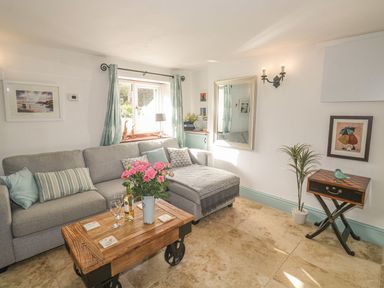 A living room with a gray sectional sofa and a wooden coffee table with flowers and wine glasses at Nightingale Cottage in Lostwithiel