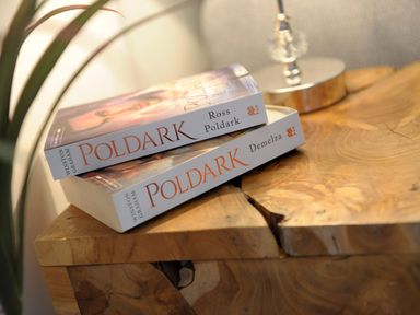 Two Poldark books titled Ross Poldark and Demelza on a wooden table next to a lamp at Nightingale Cottage in Lostwithiel