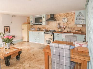 A kitchen with blue cabinets a wooden dining table and checked chairs at Nightingale Cottage in Lostwithiel