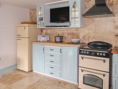 A kitchen with a cream refrigerator blue cabinets a TV a radio a slow cooker a bowl and a stove at Nightingale Cottage in Lostwithiel