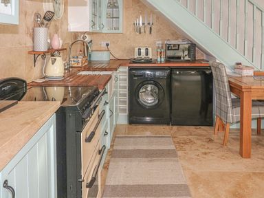 A kitchen with a stove a washing machine a dishwasher a microwave and a dining table at Nightingale Cottage in Lostwithiel