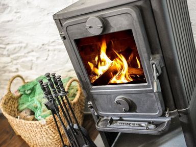 A wood burning stove with tools and a wicker basket filled with logs at Nightingale Cottage in Lostwithiel