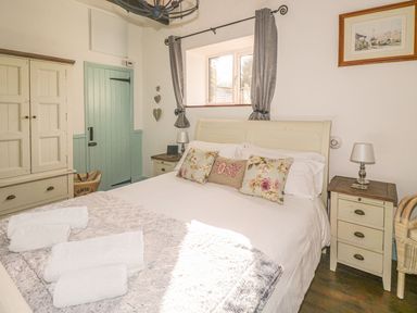 A bedroom with a bed with floral pillows bedside tables a cupboard and a window with curtains at Nightingale Cottage in Lostwithiel