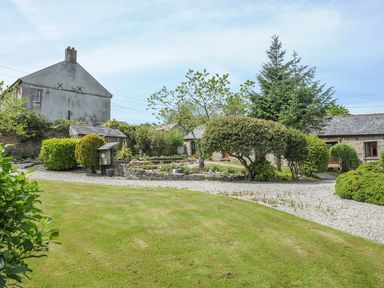 A courtyard with trimmed bushes gravel paths and grass at Nightingale Cottage in Lostwithiel