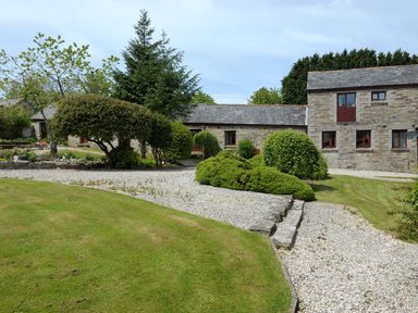 A gravel pathway with trimmed bushes and trees leading to stone buildings with slate roofs at Nightingale Cottage in Lostwithiel
