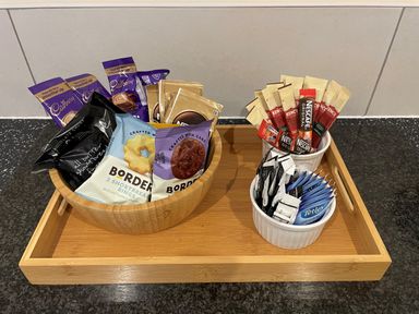 A wooden tray with assorted snacks and drink sachets on a kitchen countertop at Pams House in Weymouth